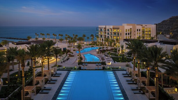Ein Resort mit großem Schwimmbad, Palmen und Blick auf den Ozean.