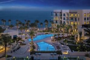 A resort pool area with a curved pool, palm trees, and a view of the ocean. - Address Beach Resort Fujairah (Al Aqah)