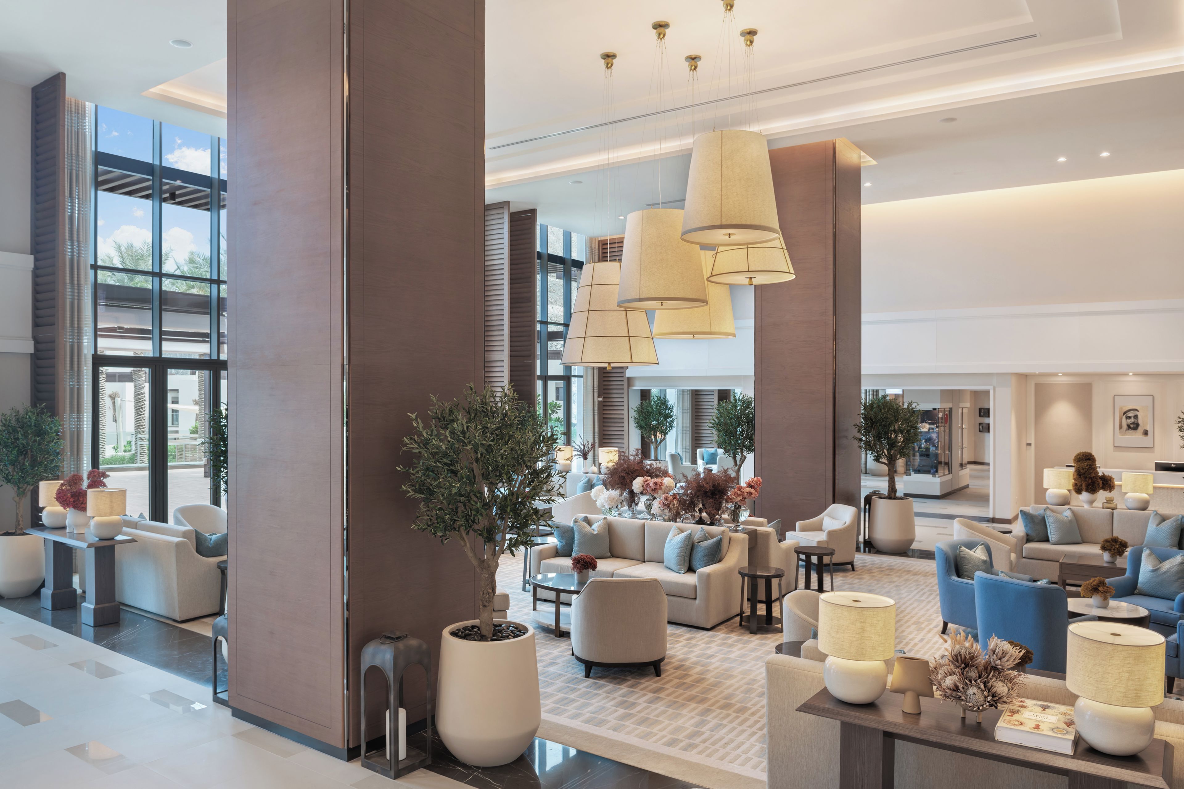 A spacious lobby with multiple seating areas, large windows, and modern lighting fixtures.