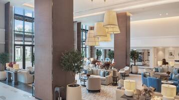 A spacious lobby with multiple seating areas, large windows, and modern lighting fixtures.