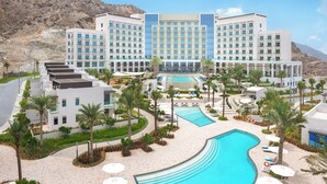A hotel with a pool, palm trees, and a mountainous backdrop. - Address Beach Resort Fujairah (Al Aqah)