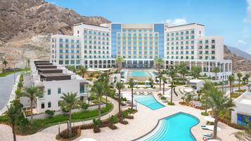 A hotel with a pool, palm trees, and a mountainous backdrop.