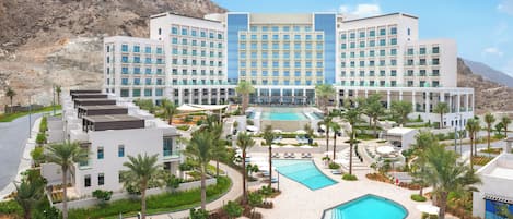 A hotel with a pool, palm trees, and a mountainous backdrop.