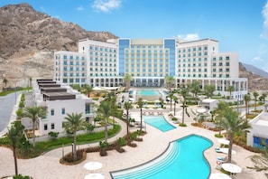 Un hôtel doté d’une piscine, de palmiers et situé au pied d’une chaîne de montagnes.