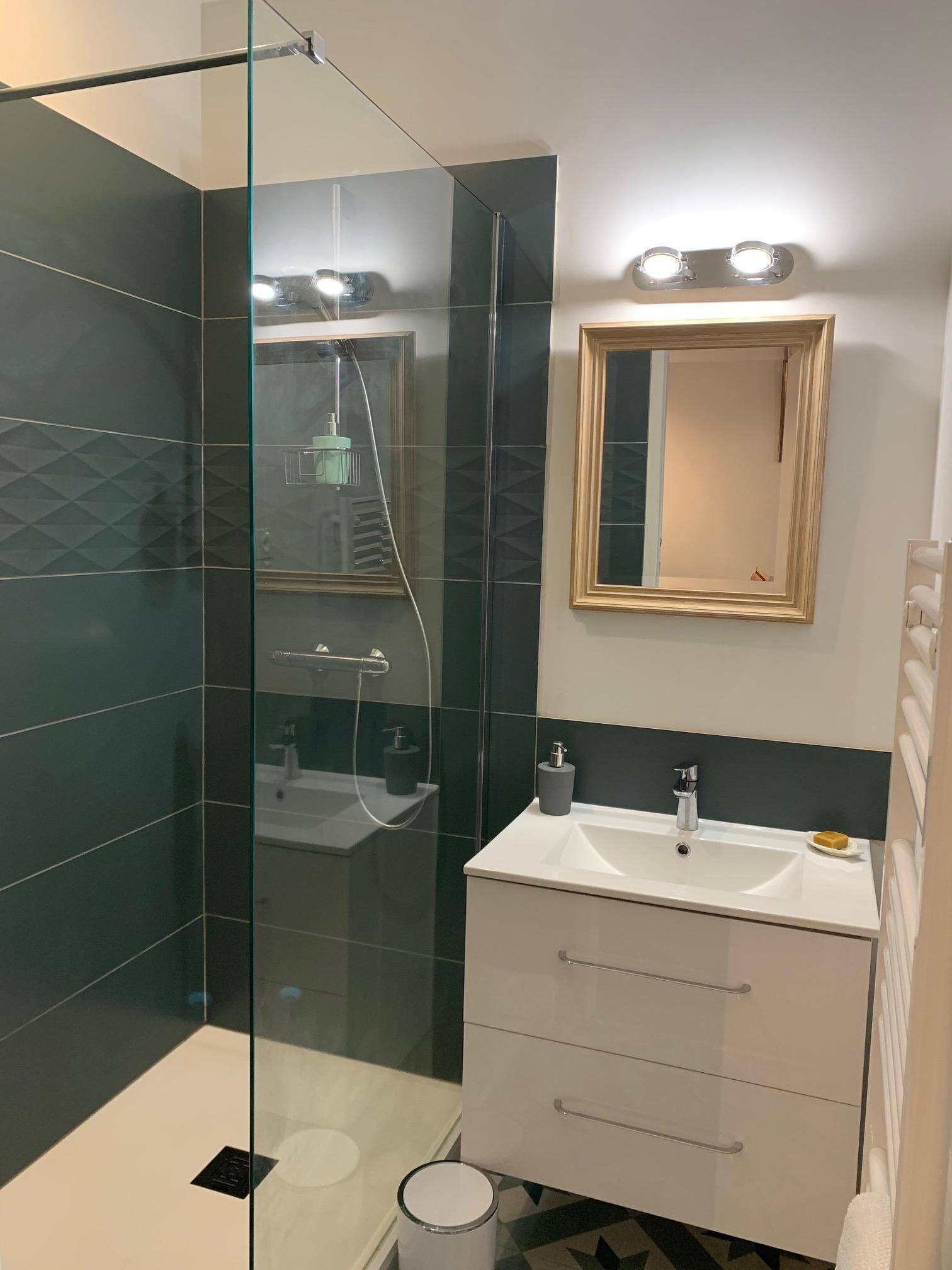 A modern bathroom with a glass shower enclosure, a white vanity with a mirror, and a small sink.