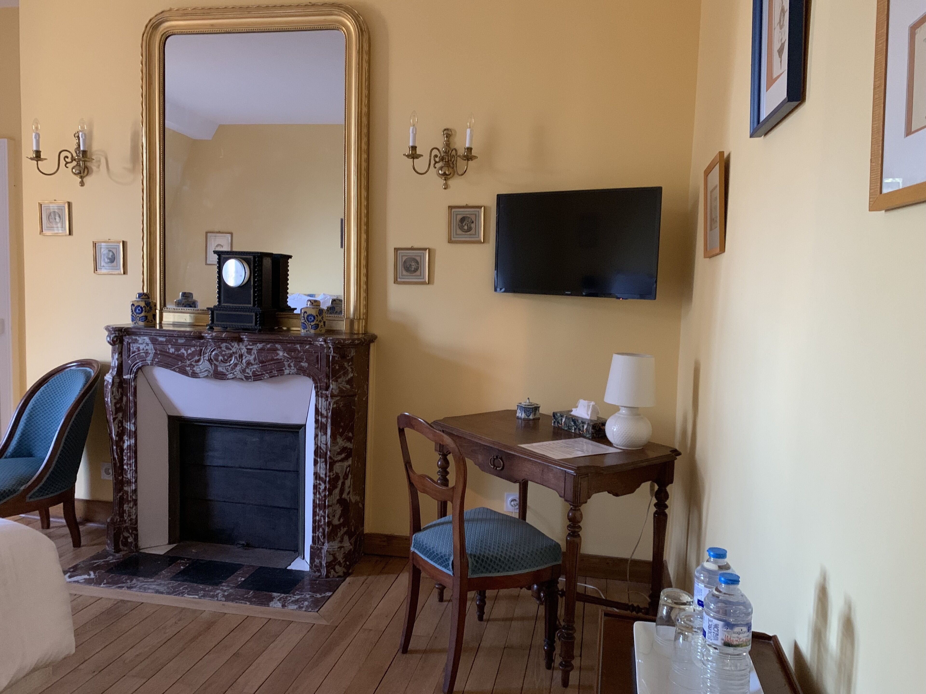 Una habitación con chimenea, televisión montada en la pared, una mesa de comedor con sillas y un espejo con marco decorativo.