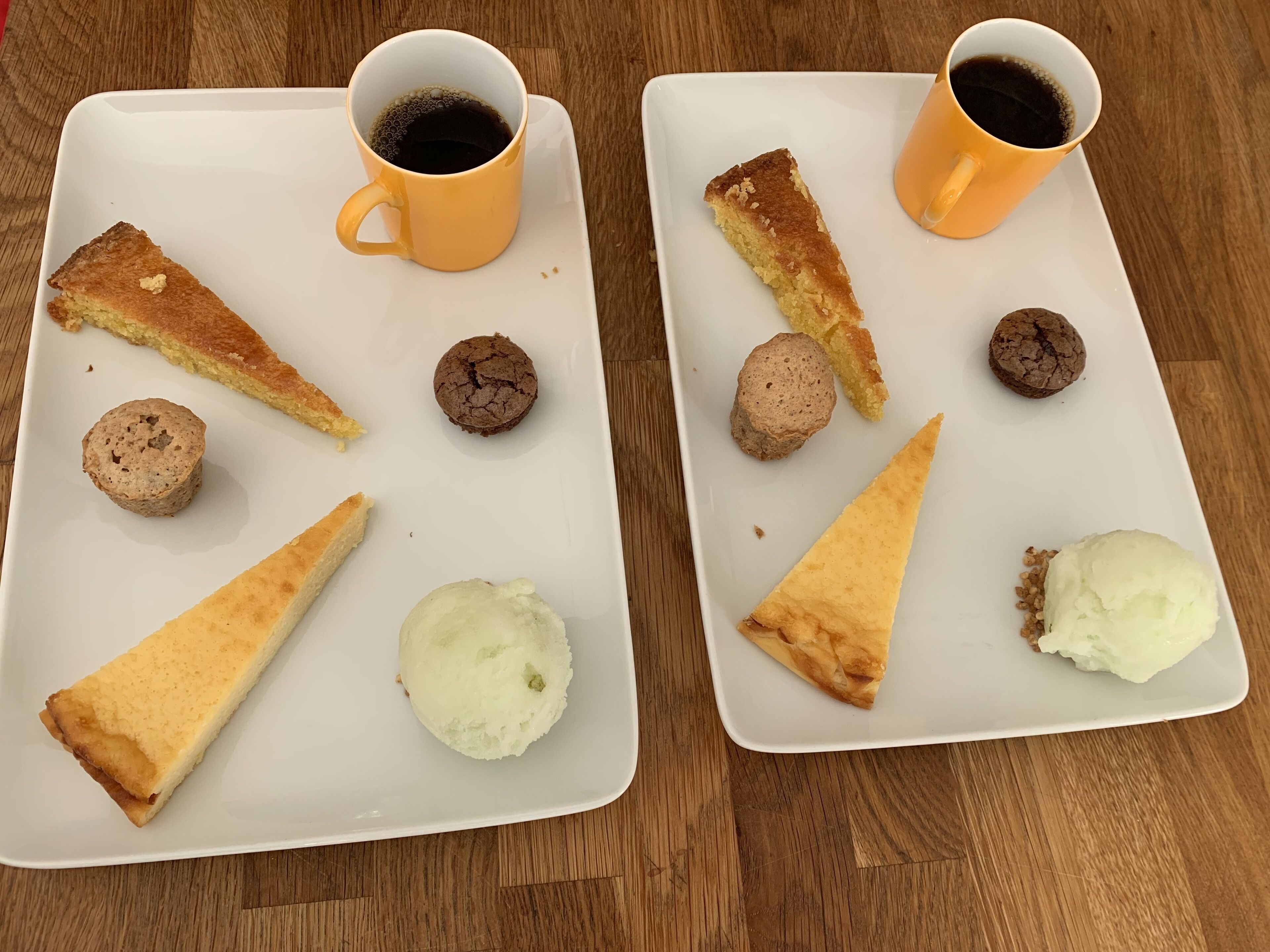 Dos platos rectangulares blancos con comida y dos tazas de café amarillas sobre una mesa de madera.