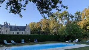 A swimming pool with lounge chairs, a hedge, and a large building in the background. - L'abeaupinière (Reboursin)