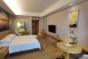 A hotel room with a bed, bedside table, a round table with a lamp, a TV mounted on the wall, and a painting. - Vienna International Hotel (Dongguan Hongmei Town) (Dongguan)