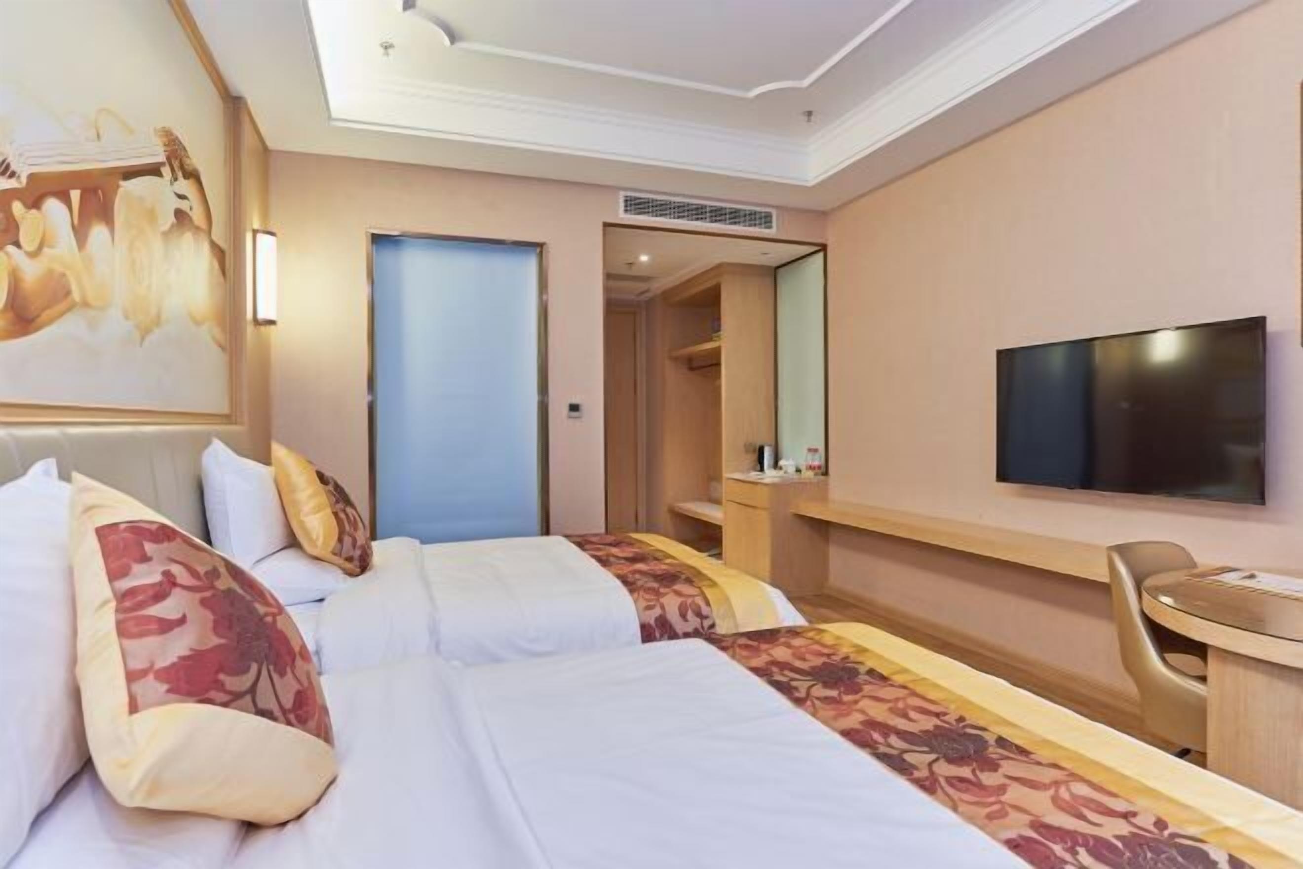 A hotel room with two beds, a desk, a chair, a television, and a door leading to a bathroom.