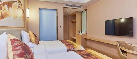 Ein Hotelzimmer mit zwei Betten, einem Schreibtisch, einem Sessel, einem Fernseher und einer Tür zu einem Badezimmer.