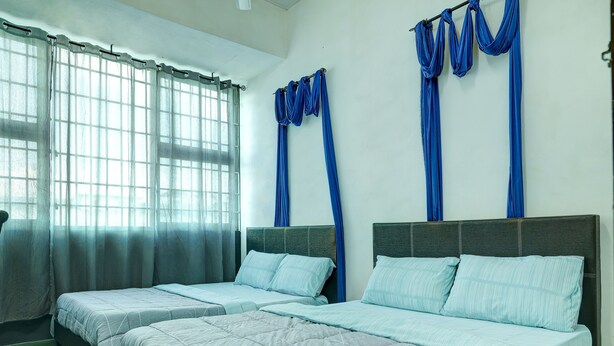Une chambre d’hôtel avec deux lits, une grande fenêtre avec des rideaux légers et des rideaux bleus aux encadrements de fenêtre.
