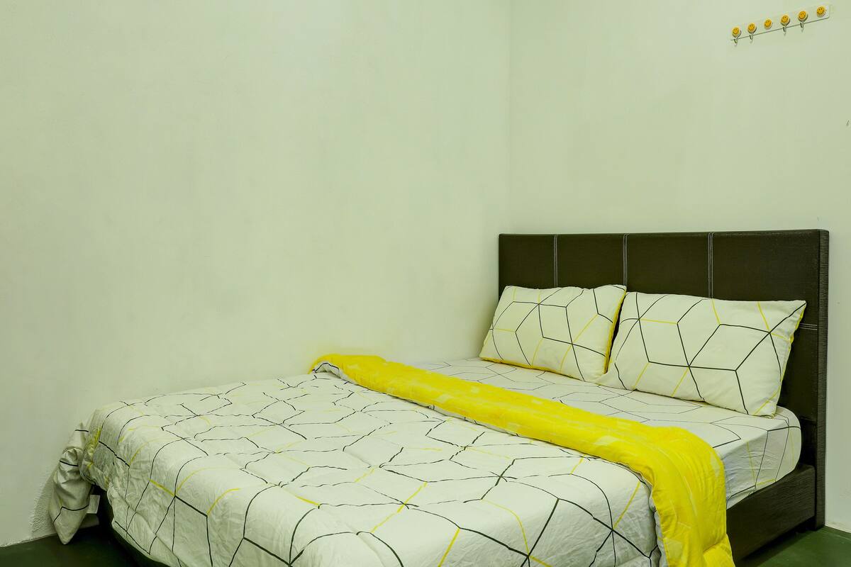 A bed with a geometric patterned bedspread and pillows, a yellow throw blanket, and a dark headboard.