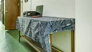 Une pièce avec une table recouverte d’une nappe à motifs de journal, un ordinateur portable et une imprimante. On peut voir un panneau avec l’inscription « SPOT ON » sur le mur.