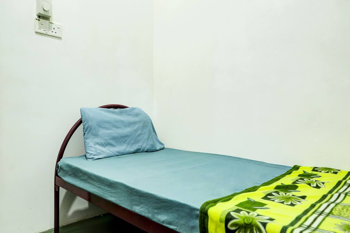 A single bed with a blue mattress and a green floral blanket.