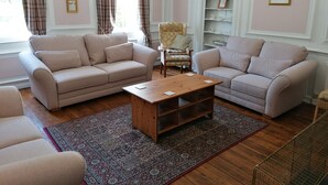A living room with two beige sofas, a wooden coffee table, a patterned rug, a chair, and a bookshelf. - Dunham House | Celebrations| Families & Friends| Parking | Dogs (Dunham on Trent)
