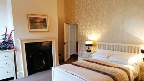 A hotel room with a white bed, a fireplace, a nightstand with a lamp, and a patterned wallpaper. - Dunham House | Celebrations| Families & Friends| Parking | Dogs (Dunham on Trent)
