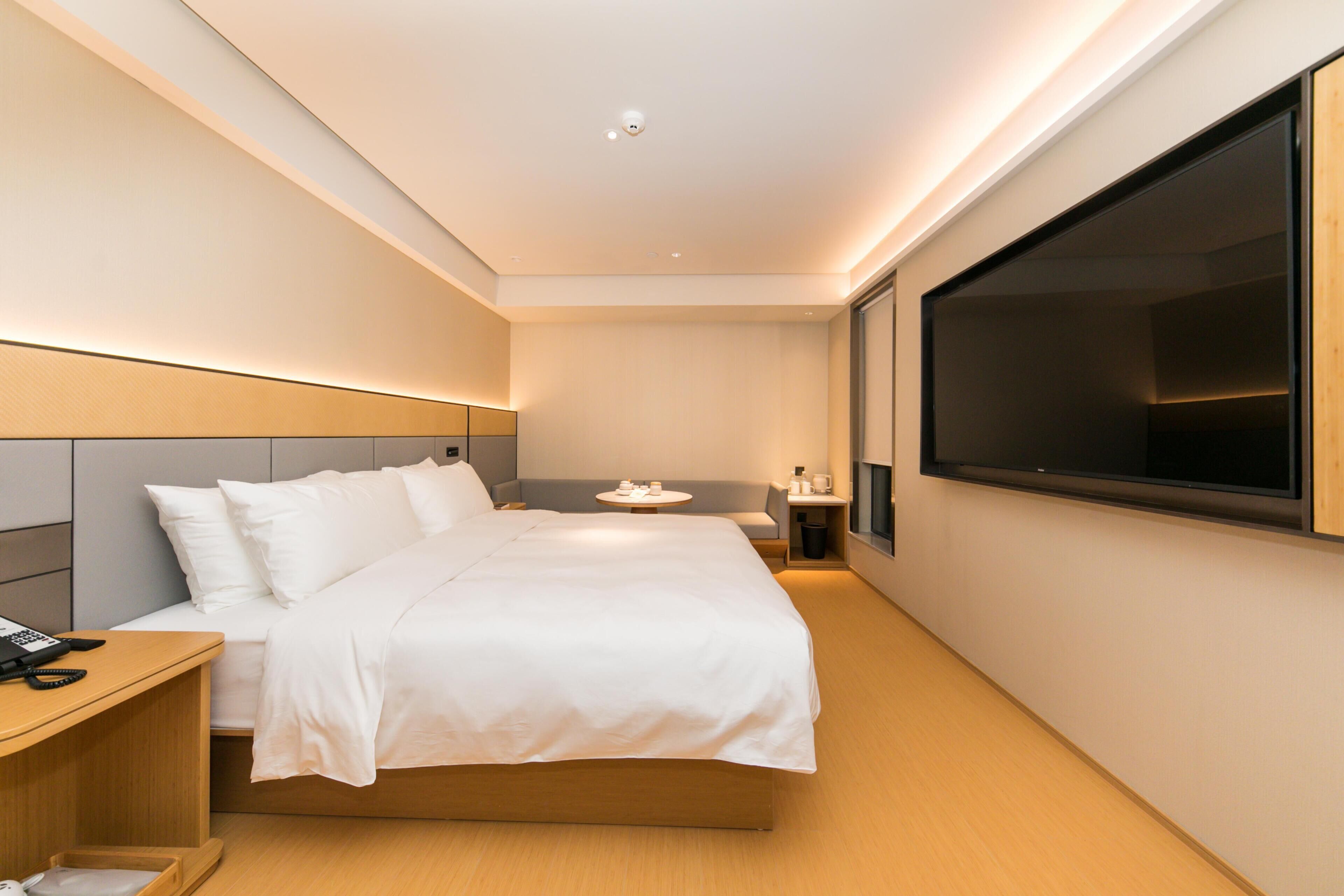 Une chambre d’hôtel moderne, dotée d’un grand lit, d’une table de chevet et d’un téléviseur à écran plat fixé au mur.