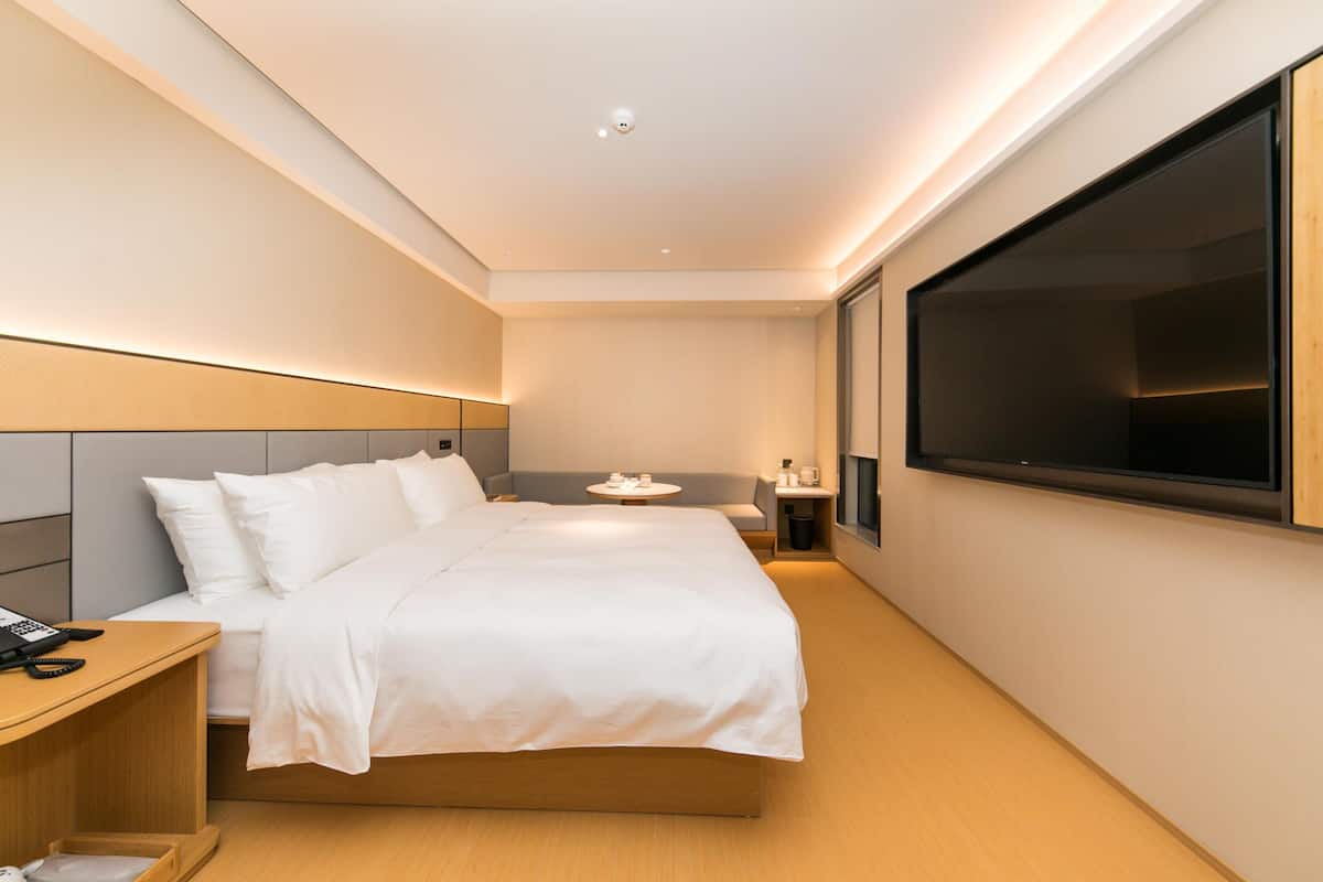 Une chambre d’hôtel moderne, dotée d’un grand lit, d’une table de chevet et d’un téléviseur à écran plat fixé au mur.