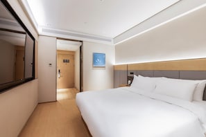 Hotellihuone, jossa on suuri sänky, yöpöytä, sängyn vieressä oleva pöytä, seinälle asennettu televisio ja ovi, joka johtaa toiseen huoneeseen.