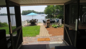 A covered patio with outdoor furniture, a grill, and a view of a lake. - Charming and spacious lakefront home with 4 bedrooms, hot tub and pool table! (Farmington)