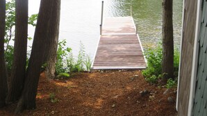 A wooden dock leading to a calm lake, surrounded by trees and a shed. - Charming and spacious lakefront home with 4 bedrooms, hot tub and pool table! (Farmington)