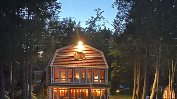 A wooden house with a porch, surrounded by trees and a body of water. - Charming and spacious lakefront home with 4 bedrooms, hot tub and pool table! (Farmington)