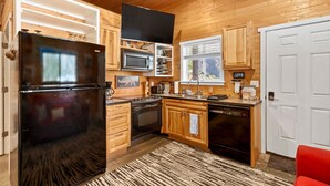 A compact kitchen with wooden cabinets, a black refrigerator, a microwave, a stove, and a dishwasher.