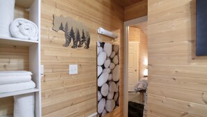 A wooden cabin interior with a shelf of neatly folded towels, a wall with a bear silhouette, and a wall-mounted towel rack.
