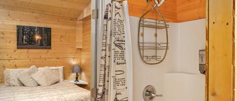 A wooden cabin bedroom with a bed, a nightstand, a framed picture on the wall, and a shower with a shower curtain.