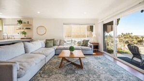 Ein modernes Wohnzimmer mit einer Eckcouch, einem Holztisch und einem großen Fenster mit Blick ins Freie.