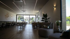 A modern cafe with a wooden floor, tables, chairs, and a large window offering a view of the outdoors.