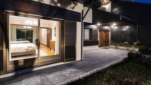 A modern house with a large sliding glass door leading to a bedroom with a bed and dresser.