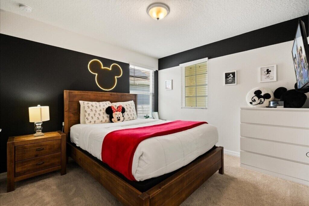 A bedroom with a wooden bed, a nightstand, a dresser, and Mickey Mouse-themed decor.