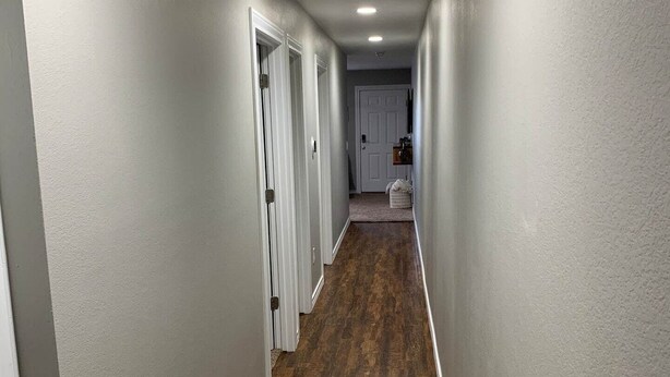 Um corredor com paredes cinzentas e soalho de madeira, que conduz a uma porta no final.