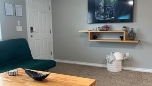Uma sala de estar com mesa de centro de madeira, sofá verde, TV fixada na parede e ventilador de teto.