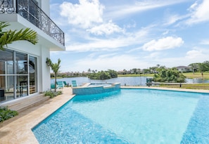 A swimming pool with a view of a lake, surrounded by a white building with a balcony.