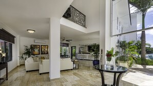 A spacious living area with a high ceiling, a dining table with a glass top, and a view of the outdoor garden. - Amazing Private Villa with Chef & Maids (Punta Cana)