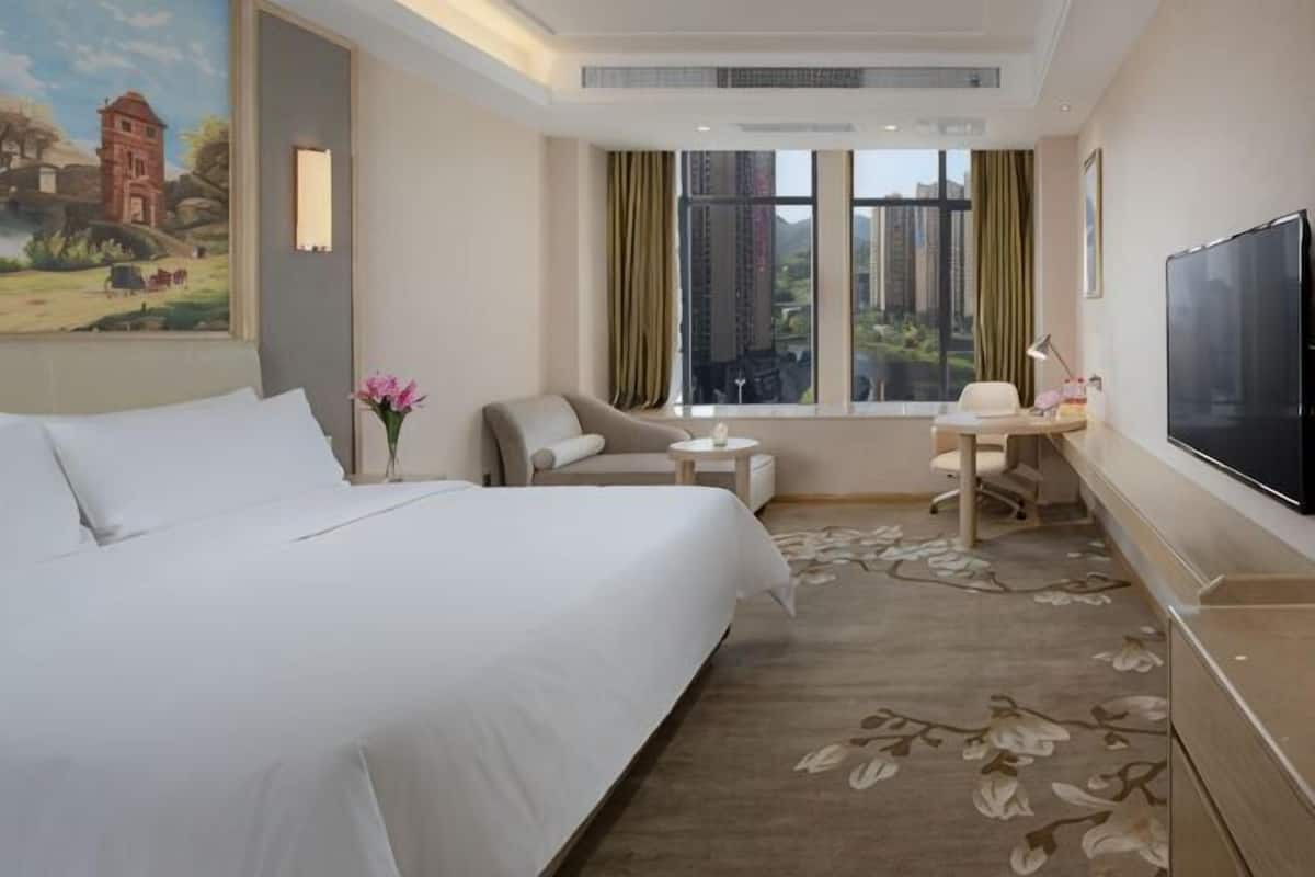 A hotel room with a large bed, a desk, a chair, a TV, and a window with a view.