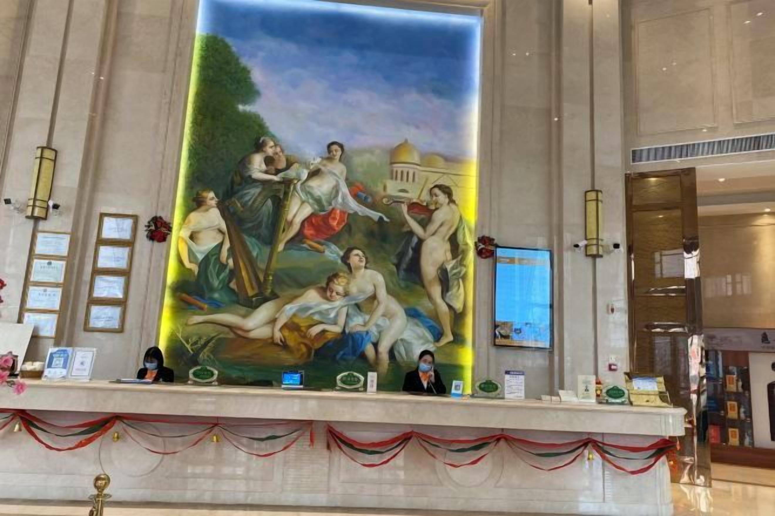 A large mural with classical figures, a reception desk, and a framed certificate on the wall.