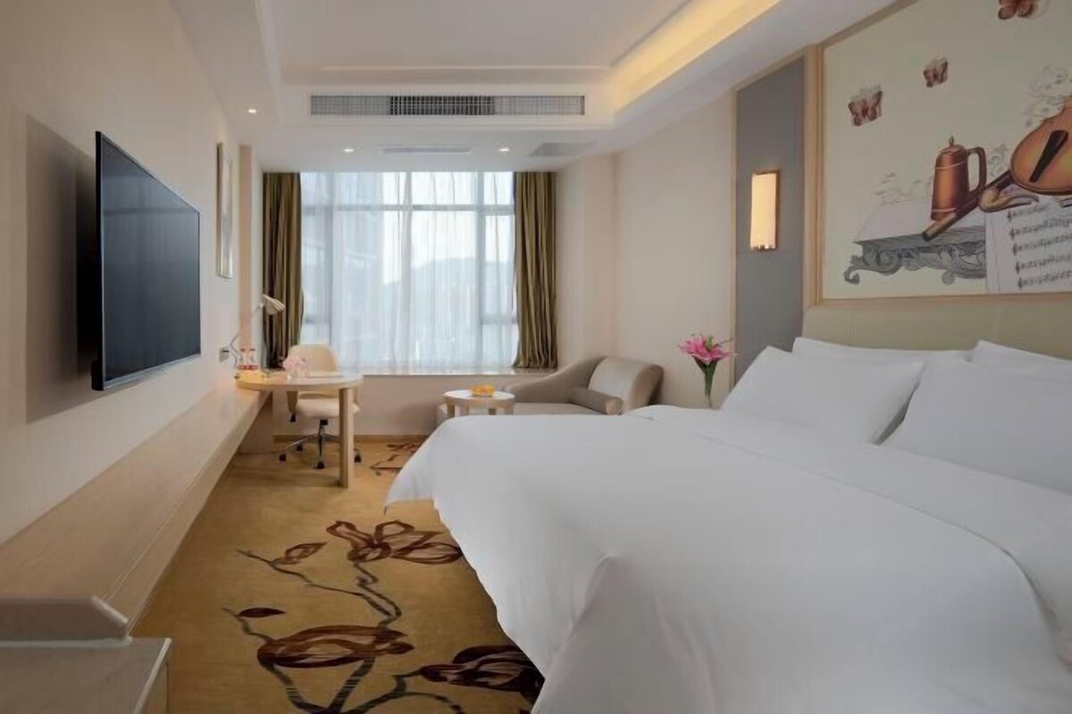 Habitación de hotel con una cama grande, un escritorio, una silla, un televisor y una ventana con cortinas.