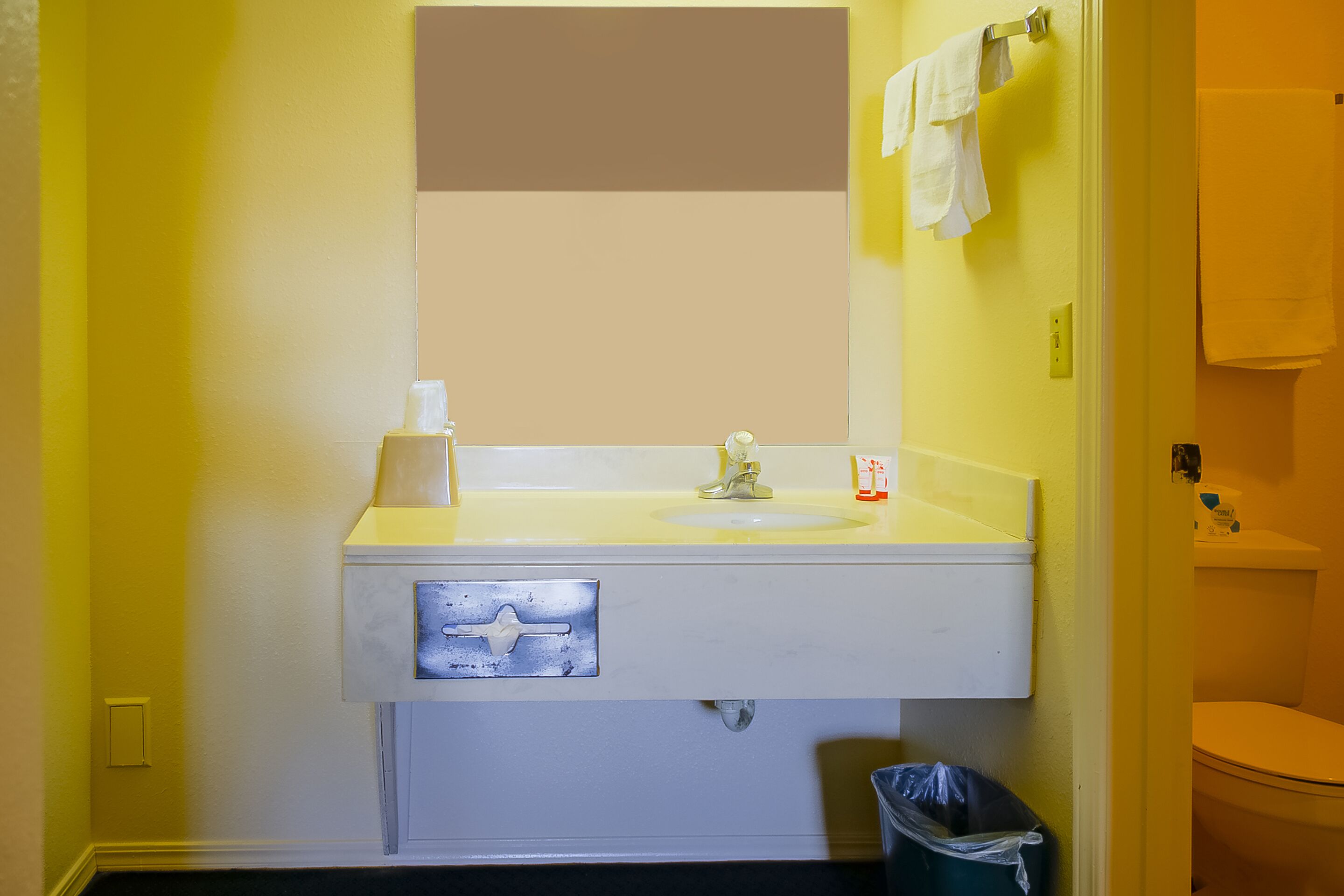 A bathroom with a yellow wall, a white sink, a mirror, and a toilet.