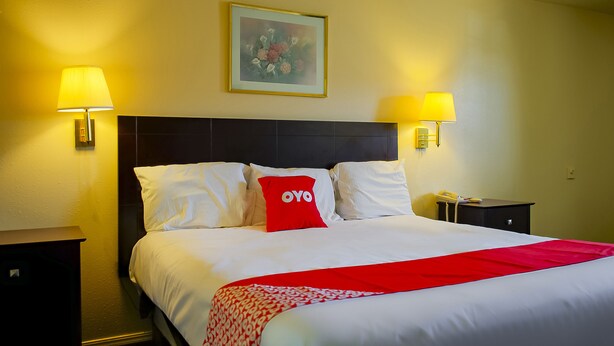 A hotel room with a bed, two bedside lamps, a nightstand, and a framed picture on the wall.