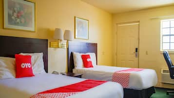 A hotel room with two beds, each with a red and white bedspread, a headboard, bedside lamps, and a door.