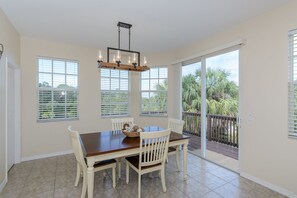Enjoy meals in this dining area with a wooden table and comfortable chairs, surrounded by large windows and a sliding door leading to an outdoor space.