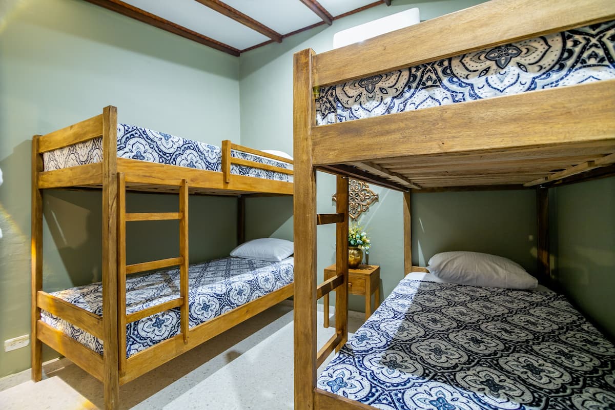 A room with two bunk beds, each with a patterned bedspread. There is a small wooden nightstand with a vase of flowers.