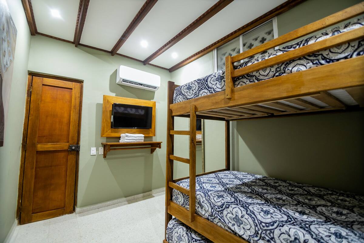A bunk bed room with a wooden door, a mounted TV, and an air conditioning unit.