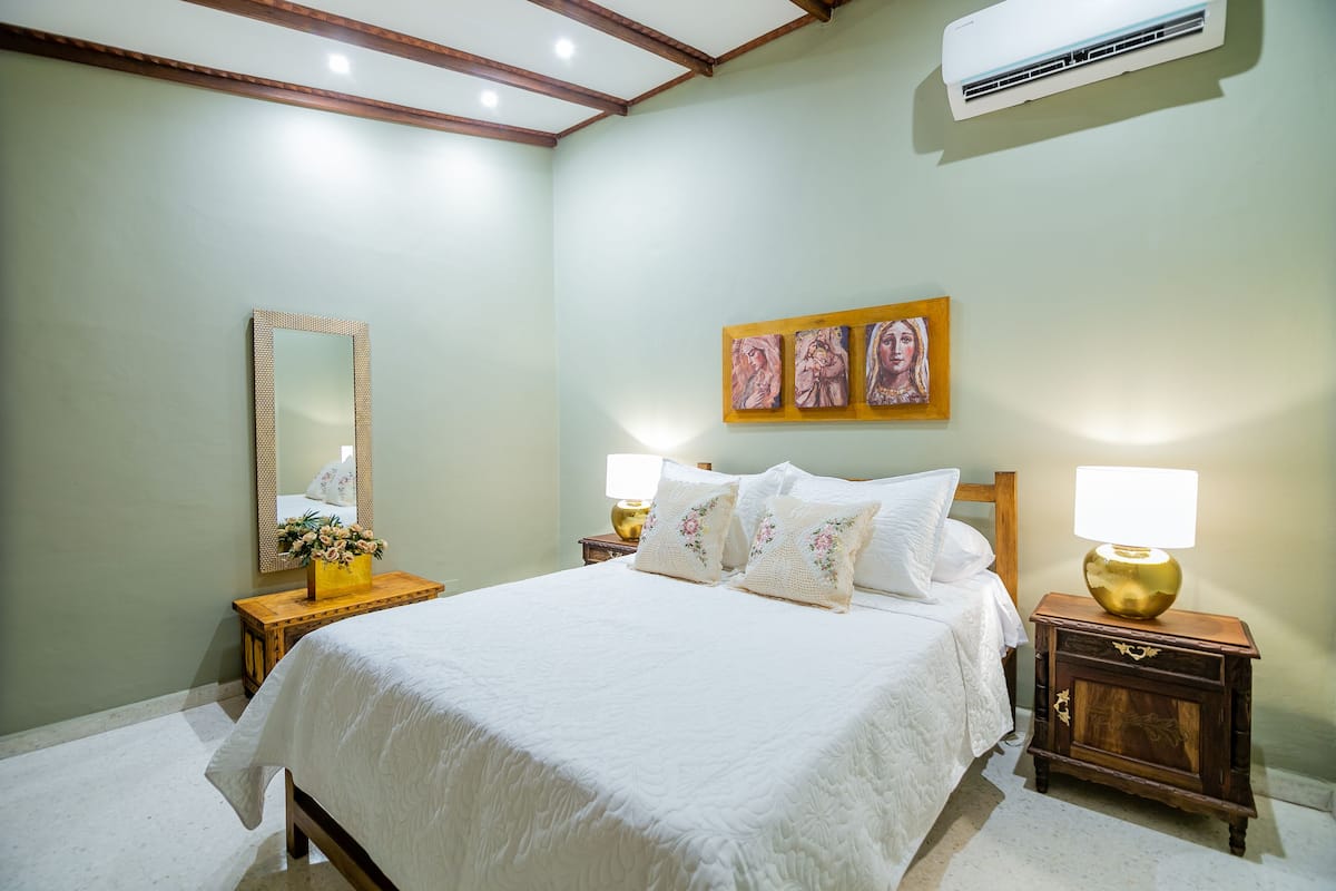 A bedroom with a bed, nightstands, a mirror, and wall art.