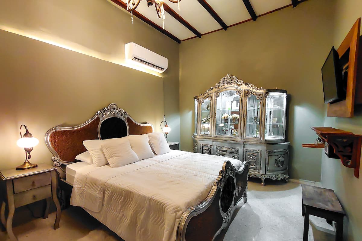 A bedroom with a large bed, a dresser with a mirror, and an air conditioning unit on the wall.