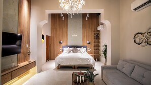 Ein modernes Schlafzimmer mit einem großen Bett, einer Kristallleuchter, einem Fernseher und einem Sofa.